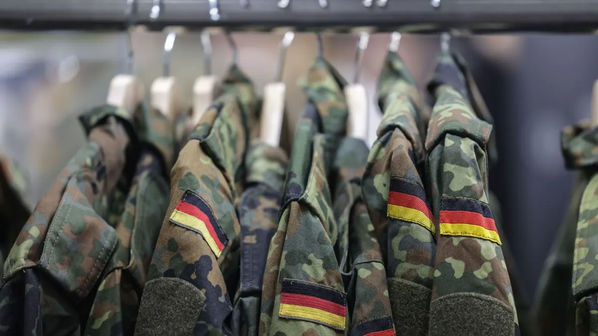 Bundeswehr: ARCHIV - 21.08.2025, Nordrhein-Westfalen, Köln: Feldjacken hängen am Stand der Bundeswehr bei der Computerspiele-Messe Gamescom (zu dpa: «CDU will Wehrpflicht-Automatismus im neuen Wehrdienst-Gesetz») Foto: Oliver Berg/dpa +++ dpa-Bildfunk +++