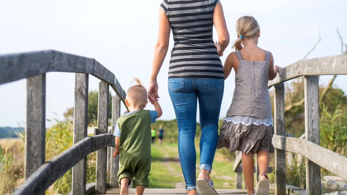 Eine Mutter läuft mit ihren Kindern über einen Steg: ILLUSTRATION - Alleinerziehend? Dann besteht in der Regel Anspruch auf Unterhalt von dem oder der Ex. (zu dpa: «Unterhalt fürs Kind: Wofür darf ich ihn verwenden?») Foto: Benjamin Nolte/dpa-tmn - Honorarfrei nur für Bezieher des dpa-Themendienstes +++ dpa-Themendienst +++