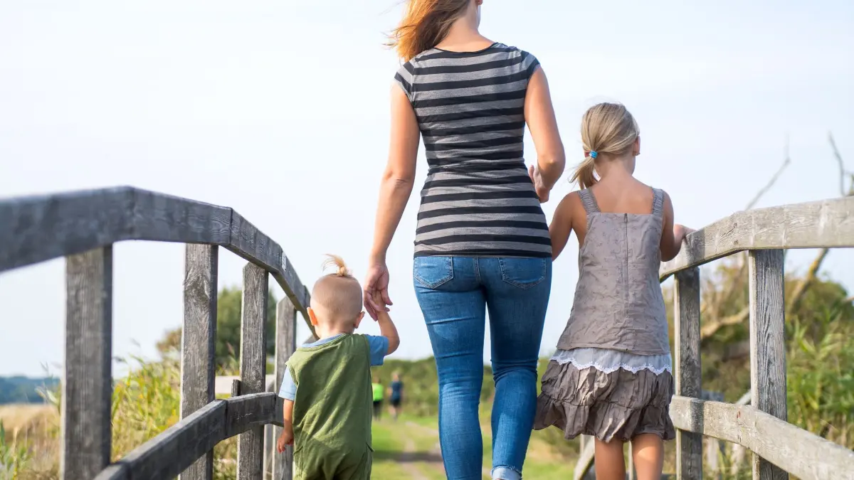 Eine Mutter läuft mit ihren Kindern über einen Steg: ILLUSTRATION - Alleinerziehend? Dann besteht in der Regel Anspruch auf Unterhalt von dem oder der Ex. (zu dpa: «Unterhalt fürs Kind: Wofür darf ich ihn verwenden?») Foto: Benjamin Nolte/dpa-tmn - Honorarfrei nur für Bezieher des dpa-Themendienstes +++ dpa-Themendienst +++