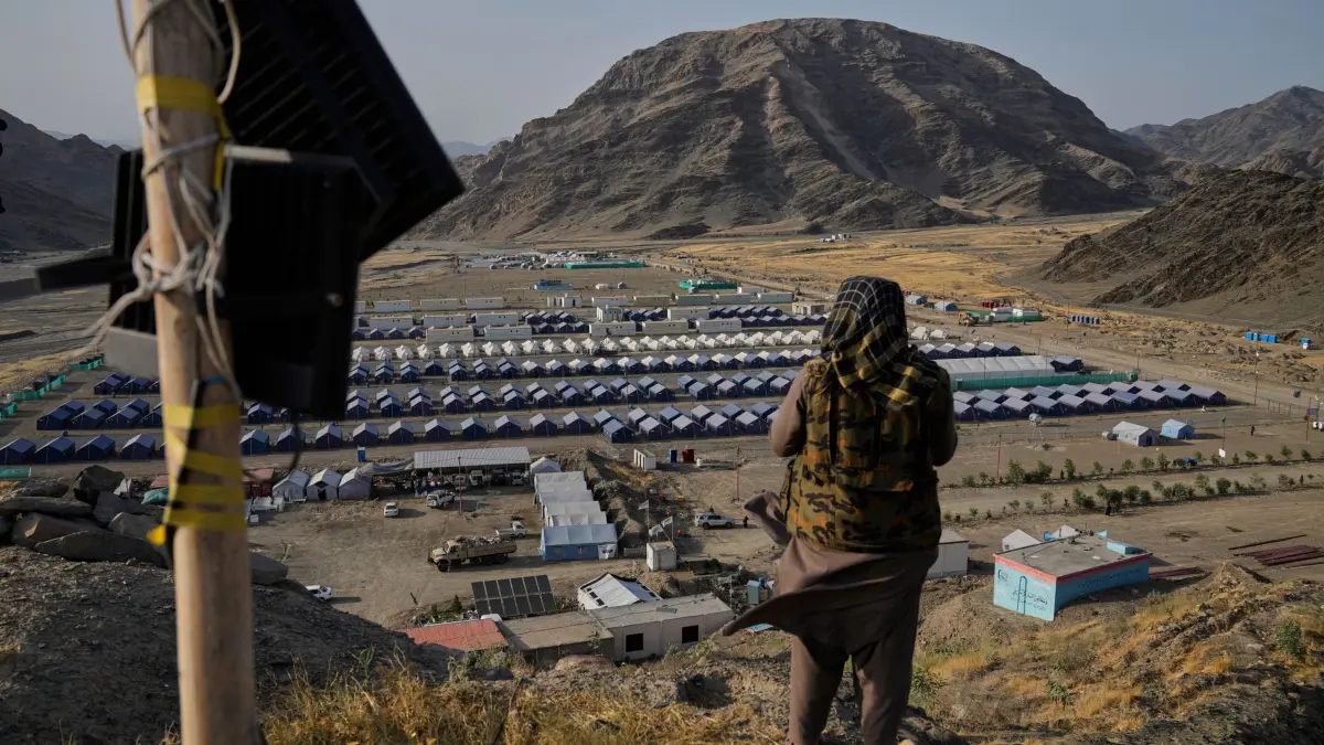 Afghanistan - Rückführung von Flüchtlingen: ARCHIV - 31.05.2025, Afghanistan, Torkham: Ein Taliban-Kämpfer steht auf einem Hügel mit Blick auf ein Lager, in dem afghanische Flüchtlinge untergebracht sind, die aus Pakistan zurückgeführt wurden, nahe der pakistanisch-afghanischen Grenze in Torkham, Afghanistan. (zu dpa: «UN-Organisation sieht Afghanistan-Abschiebungen kritisch») Foto: Ebrahim Noroozi/AP/dpa +++ dpa-Bildfunk +++
