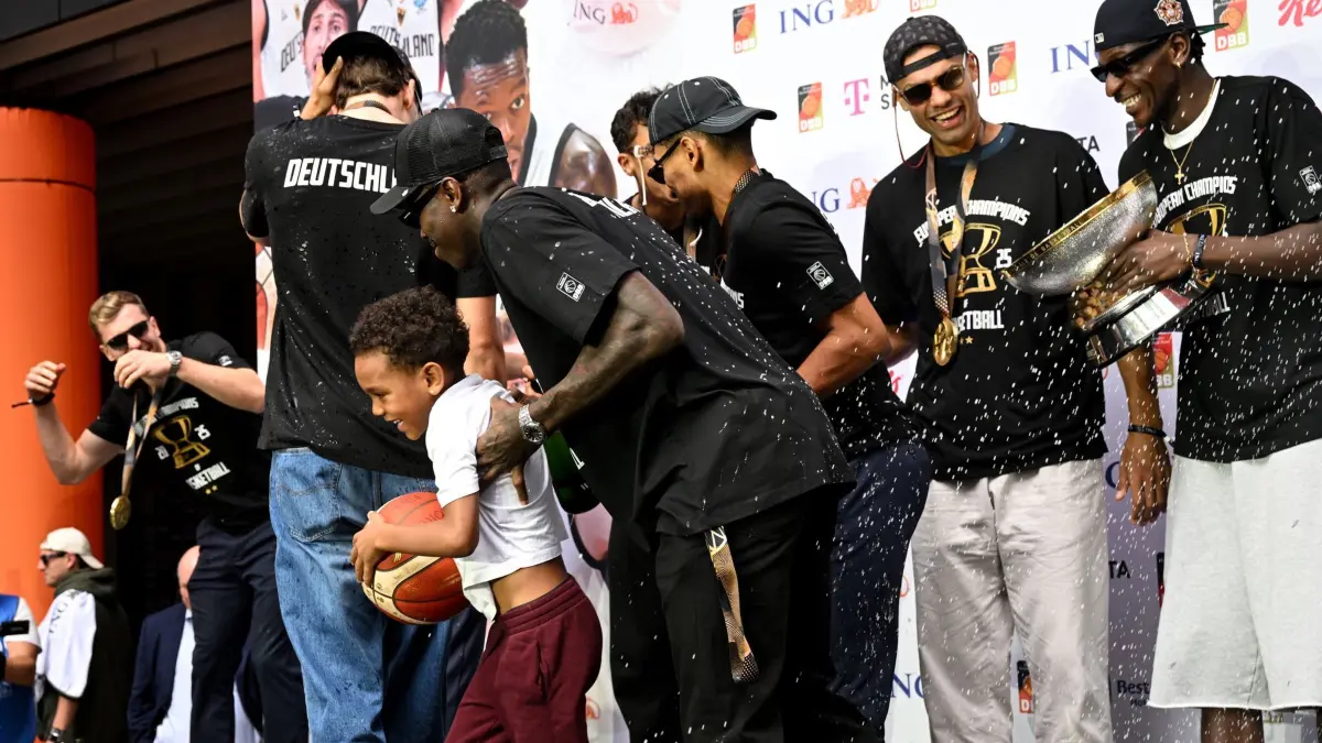 Empfang Basketball-Nationalmannschaft nach Titelgewinn: 15.09.2025, Hessen, Frankfurt/Main: Basketball: EM, Deutschland, nach dem Titelgewinn, Empfang des deutschen Teams, Dennis Schröder (M/Deutschland) versucht seinen Sohn vor einer Sektdusche zu schützen. Foto: Boris Roessler/dpa - ACHTUNG: Nur zur redaktionellen Verwendung im Zusammenhang mit der aktuellen Berichterstattung und nur mit vollständiger Nennung des vorstehenden Credits +++ dpa-Bildfunk +++