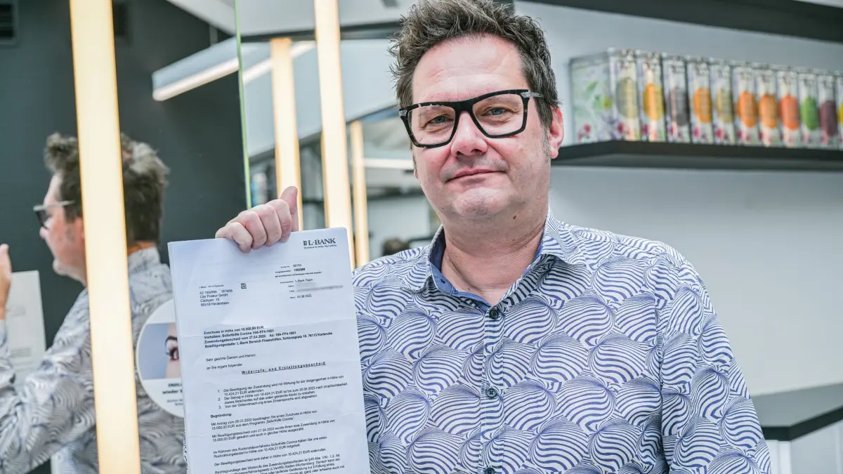 Friseur Holger Schier: ARCHIV - 25.09.2025, Baden-Württemberg, Heidenheim: Friseur Holger Schier steht in seinem Friseursalon in Heidenheim an der Brenz und hebt den Corona-Soforthilfe-Rückzahlungsbescheid hoch, gegen den er vorgegangen ist. Sein Fall ist beispielhaft für zahlreiche Unternehmer in Baden-Württemberg, die aufgefordert werden, die Hilfen an den Staat zurückzahlen. (zu dpa: «Friseur gewinnt im Streit um Corona-Hilfe») Foto: Jason Tschepljakow/dpa +++ dpa-Bildfunk +++
