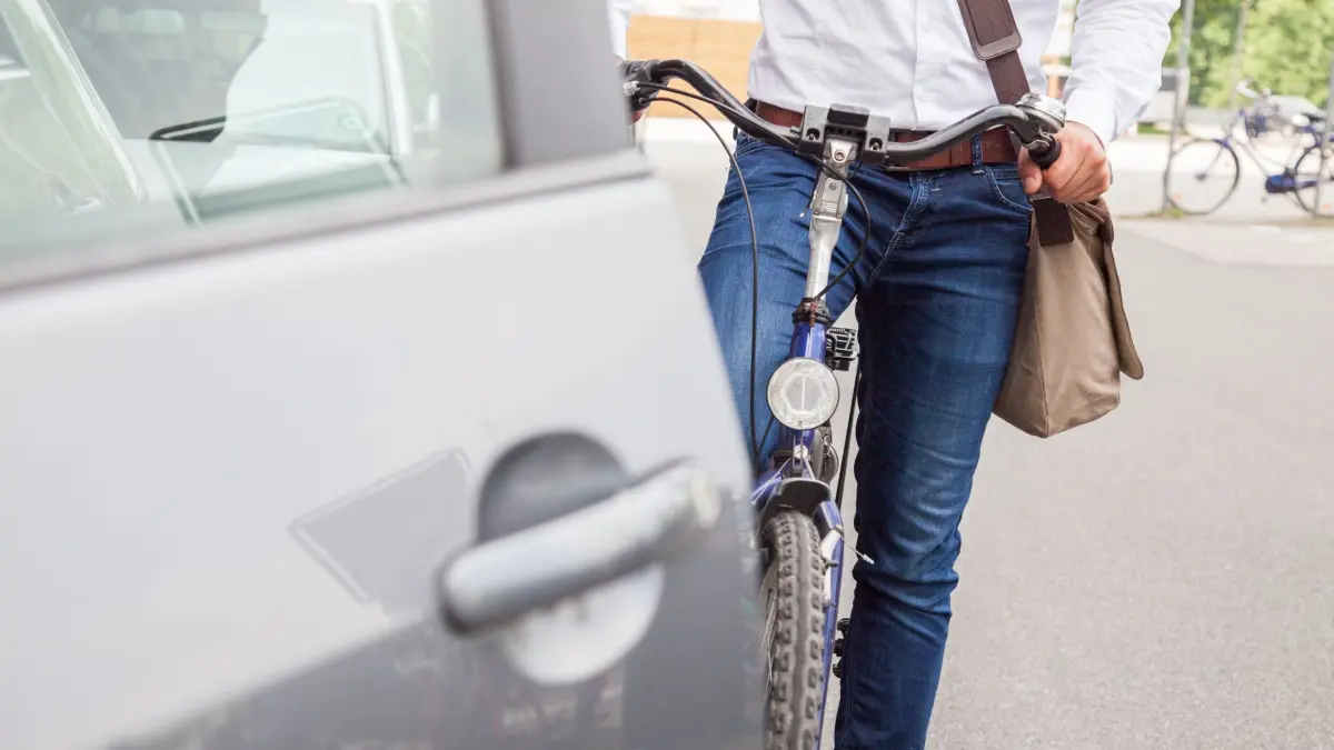 Radfahrer hält vor geöffneter Autotür: ILLUSTRATION - Viele Radwege führen an parkenden Autos vorbei. Mit Rücksicht und dem «Holländischen Griff» sinkt die Gefahr von sogenannten Dooring-Unfällen. (zu dpa: ««Holländischer Griff»: Tür-Unfälle mit Radlern vermeiden») Foto: Christin Klose/dpa-mag - Honorarfrei nur für Bezieher des Dienstes dpa-Magazin +++ dpa-Magazin +++