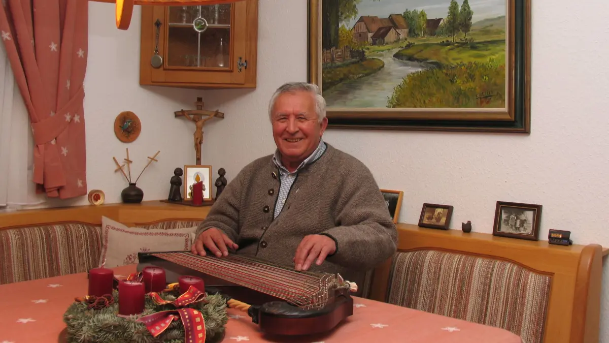 Ernst Heller in seinem Atelier an der Zither. Das Bild im Hintergrund hat er selbst gemalt.