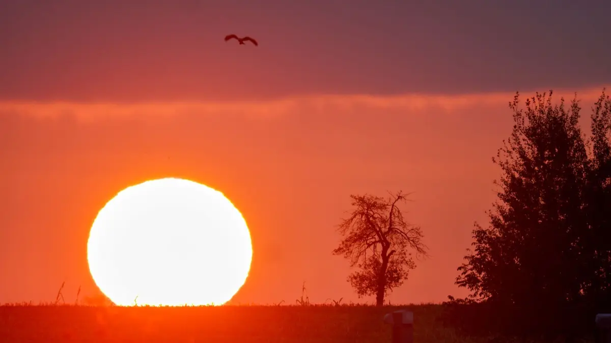 Wetter in Baden-Württemberg: 12.10.2025, Baden-Württemberg, Biberach an der Riß: Die Sonne geht am Morgen bei Biberach an der Riß auf und färbt den Himmel in Rottönen. Foto: Thomas Warnack/dpa +++ dpa-Bildfunk +++