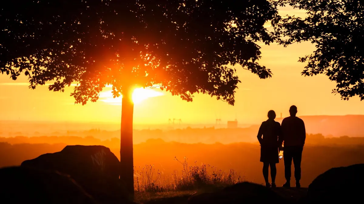Ein Paar steht bei Sonnenaufgang auf einem Berg: ILLUSTRATION - Bei der quälenden Frage, ob man sich nach dem Verlust neu verlieben darf, kann es helfen, sich vorzustellen, was der oder die Verstorbene dazu sagen würde. (zu dpa: «Eine neue Beziehung im Trauerjahr: Okay oder problematisch?») Foto: Julian Stratenschulte/dpa/dpa-tmn - Honorarfrei nur für Bezieher des dpa-Themendienstes +++ dpa-Themendienst +++