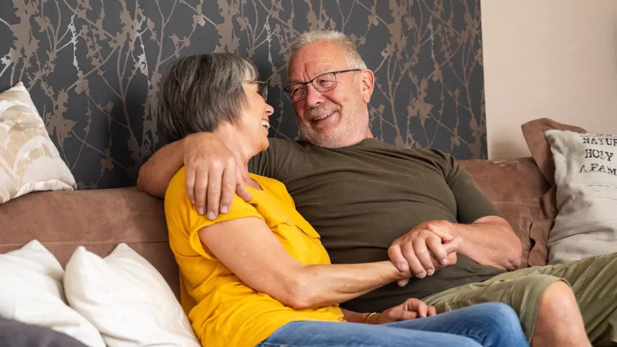 Älteres Paar sitzt lächelnd auf einer Couch: ILLUSTRATION - Der Witwer hat eine neue Partnerin gefunden. Auch Angehörige merken dann oft, dass das ihr Leben ebenfalls wieder erleichtert. (zu dpa: «Neue Liebe nach Verlust: Reaktion oft positiver als gedacht») Foto: Benjamin Nolte/dpa-mag - Honorarfrei nur für Bezieher des Dienstes dpa-Magazin +++ dpa-Magazin +++