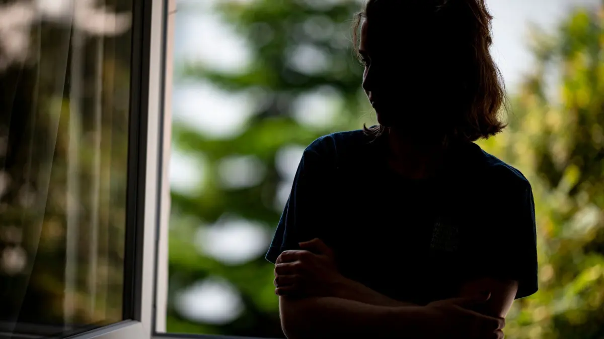 Illustration - Einsamkeit: PRODUKTION - 13.07.2021, Berlin: ILLUSTRATION - Eine Frau steht mit verschränkten Armen in ihrer Wohnung an einem Fenster. (gestellte Szene) (zu dpa: «Armut macht einsam – wenn Teilhabe am Leben zu teuer wird») Foto: Fabian Sommer/dpa +++ dpa-Bildfunk +++