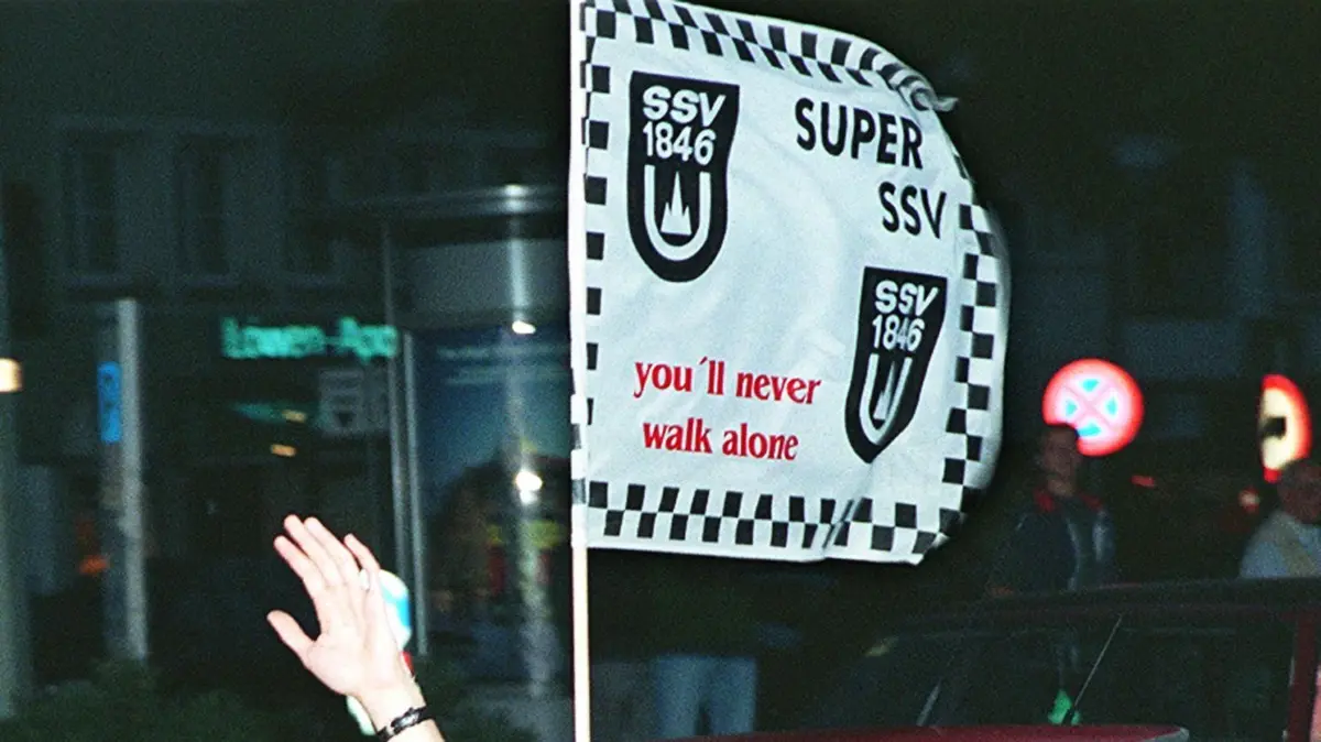 Ulm, SSV Ulm 1846, Aufstieg in die 1. Bundesliga: Jubelnde Fans fahren durch die Ulmer Innenstadt. Sie halten eine Fahne aus dem Fenster mit der Aufschrift: "Super SSV, you'll never walk alone". Der SSV Ulm 1846 spielt in der kommenden Saison in der 1. Bundesliga. Am letzten Spieltag der 2. Liga reichte dem SSV zu Hause gegen Greuther Fürth ein torloses Unentschieden, um den Durchmarsch ins Oberhaus zu schaffen.