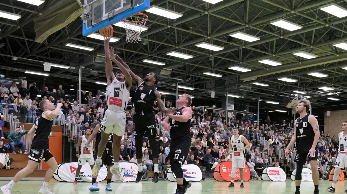 Basketball RL | TSG Solcom Ravens Reutlingen vs. Lich Basketball: Basketball 1. RL | TSG Solcom Ravens Reutlingen (weiss) vs. Lich Basketball (schwarz) // 2025-10-25 // Foto: Joachim Baur // #21 Milew Mallory (TSG Reutlingen) am Korb / volle Oskar-Kalbfell-Halle / #1 Phillip Ryan Flowers (Lich) / #13 Johannes Lischka (Lich)