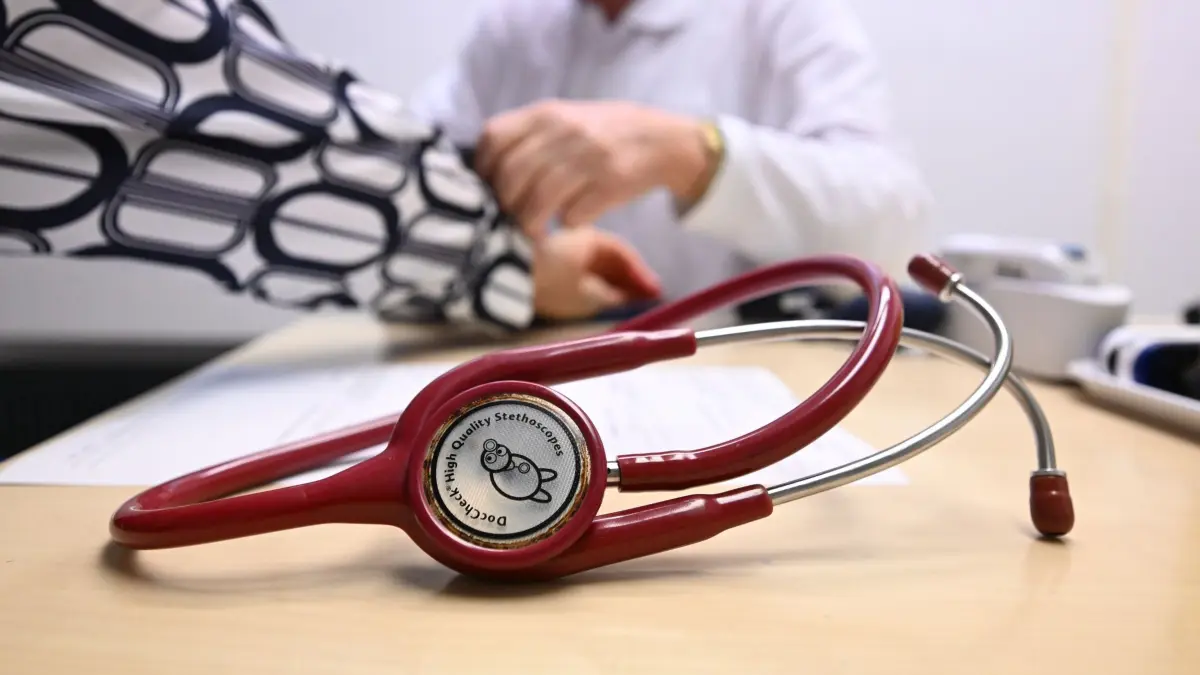 Ärztliche Bereitschaftspraxis: SYMBOLBILD - 16.10.2024, Baden-Württemberg, Leonberg: Ein Arzt misst in einer Bereitschaftspraxis in einem Krankenhaus in einem Untersuchungsraum bei einer Patientin den Blutdruck (gestellte Szene). Im Vordergrund liegt ein Stethoskop. (zu dpa: «Bei Kaffee und Kuchen über die eigene Gesundheit plaudern») Foto: Bernd Weißbrod/dpa +++ dpa-Bildfunk +++