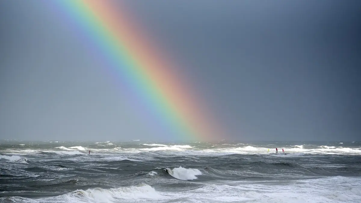 Sturmflut an der Nordsee - Insel Sylt: ARCHIV - 05.10.2025, Schleswig-Holstein, Westerland / Sylt: Surfer sind bei einer Sturmflut auf den Wellen der Nordsee vor dem Strand von Westerland auf der Nordseeinsel Sylt unter einem Regenbogen unterwegs.
Vor einem Strand der Insel Sylt sind Surfer unterwegs, trotz der Sturmflut. (zu dpa: «Nasser Norden: viel Regen im Oktober») Foto: Daniel Bockwoldt/dpa +++ dpa-Bildfunk +++