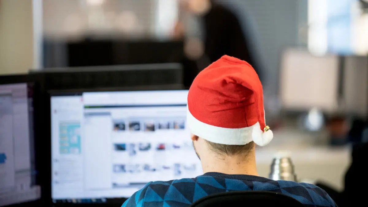 Ein Mann sitzt mit Weihnachtsmütze im Büro: ILLUSTRATION - Ob es Weihnachtsgeld gibt oder nicht, kann im Tarif- oder Arbeitsvertrag festgehalten sein. (zu dpa: «Habe ich Anspruch auf Weihnachtsgeld?») Foto: Zacharie Scheurer/dpa-mag - Honorarfrei nur für Bezieher des Dienstes dpa-Magazin +++ dpa-Magazin +++