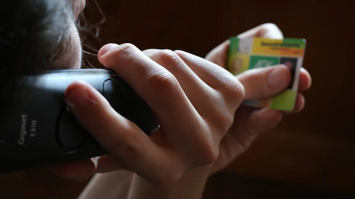 Ein Mann hält beim Telefonieren eine Gesundheitskarte in der Hand.