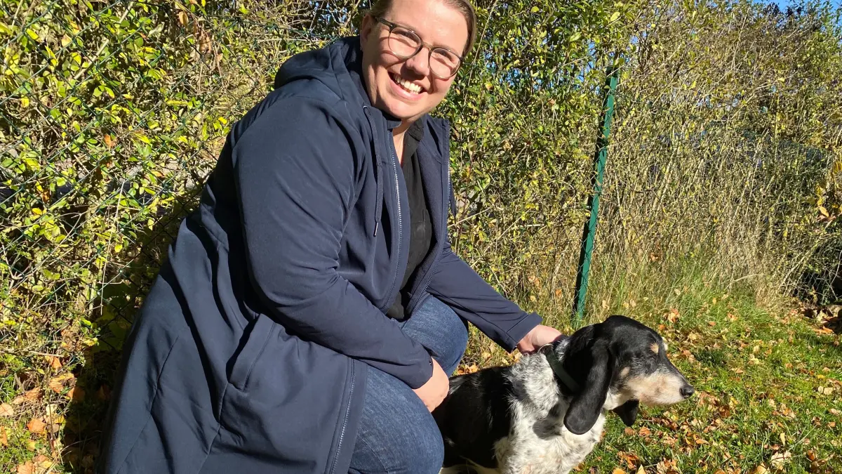 Die Schlatter Journalistin, Podcasterin, Imkerin und Jägerin Katrin Schuler mit dem Helden ihres Höradventskalenders, Feli, vor dem Gartenzaun mit dem Loch, durch das der Schweizer Niederlaufhund so gerne ausbüxt - natürlich nur in der Fantasie der Geschichtenerzählerin.