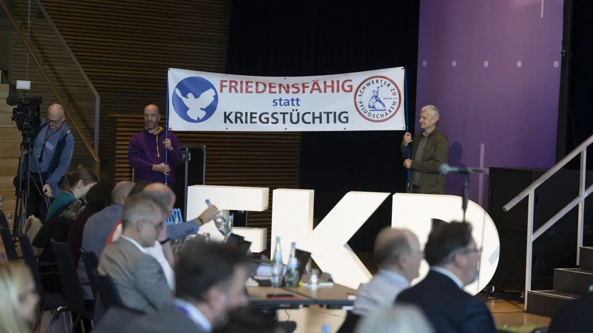 Bericht ueber die Arbeit der Friedenswerkstatt waehrend der 6. Tagung der 13. Synode der EKD in Dresden: Bericht ueber die Arbeit der Friedenswerkstatt und Vorstellung der Friedensdenkschrift des Rates der Evangelischen Kirche in Deutschland (EKD) waehrend der 6. Tagung der 13. Synode der EKD am Montag (10.11.2025) in Dresden (im Foto: Zwei Personen halten ein Banner mit der Aufschrift "Friedensfaehig statt Kriegstuechtig"). Am Montag wird bei der EKD-Jahrestagung in Dresden eine sogenannte Friedensdenkschrift der evangelischen Kirche veroeffentlicht. Das Grundsatzpapier entstand als Reaktion auf innerkirchliche Debatten nach dem russischen Ueberfall auf die Ukraine im Februar 2022. In der Folge stritten die deutschen Protestanten darueber, ob Waffenlieferungen an das ueberfallene Land aus christlicher Perspektive geboten oder abzulehnen sind. (Siehe epd-Meldung vom 10.11.2025).