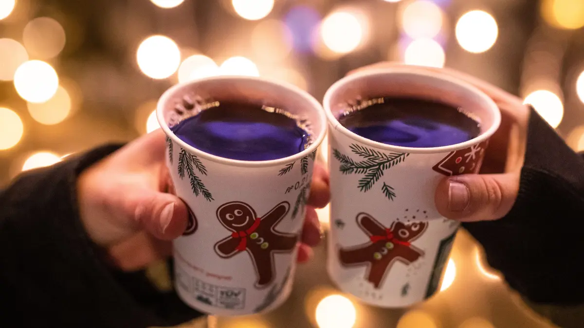 Zwei Frauen stoßen mit Glühwein gefüllten Bechern auf dem Weihnachtsmarkt an.