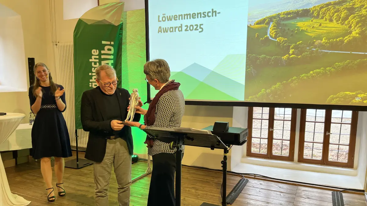 Löwenmensch Award 2025: Die stellvertretende Vorsitzende des Schwäbische Alb Tourismusverbands, Marion Leuze-Mohr, überreicht Mike Münzing den silbernen Löwenmenschen, links daneben steht die Moderatorin Jana Große Hokamp.