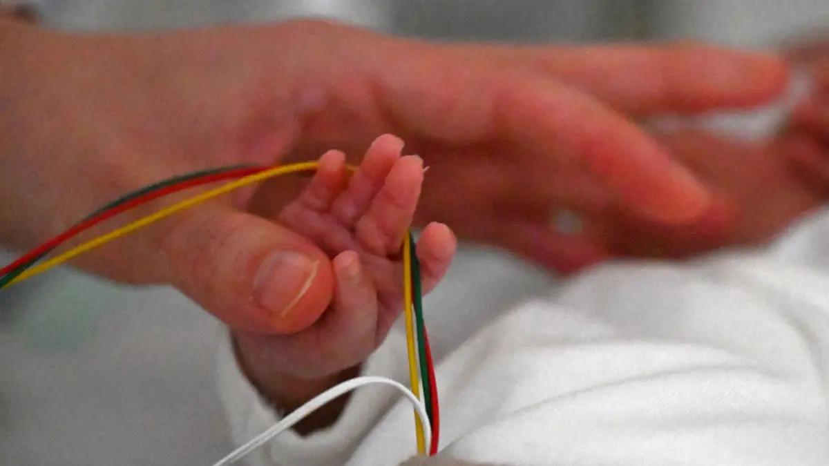 Nähen für Frühchen: PRODUKTION - 14.11.2025, Sachsen, Leipzig: Die Hand eines Frühchens, mit Kabeln umgeben wird von der Mutter im Universitätsklinikum Leipzig gehalten. Nach einer Studie aus dem Jahr 2023 wird in Deutschland fast jedes 11. Kind vor der Vollendung der 37. Schwangerschaftswoche geboren - über 60.000 Betroffene in einem Jahr. Auf ihr Schicksal will der weltweite Frühgeborenentag am 17. November aufmerksam machen. (zu dpa: «Kleine Decken mit großer Wirkung») Foto: Jennifer Brückner/dpa +++ dpa-Bildfunk +++