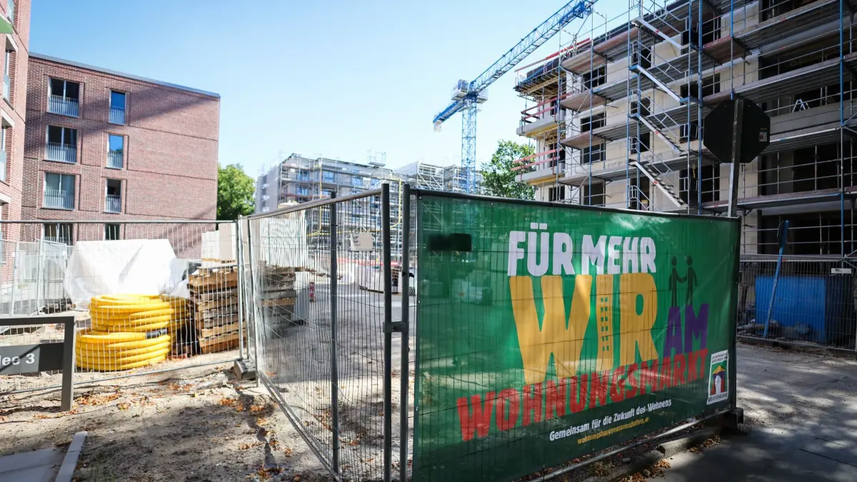 Wohnungsbau: ARCHIV - 21.08.2025, Hamburg: Die Baustelle (r) für einen weiteren Bauabschnitt einer Wohnanlage der bgfg (Baugenossenschaft freier Gewerkschafter eG) in Hamburg-Rothenburgsort. Auf dem Banner am Bauzaun steht «Für mehr Wir am Wohnungsmarkt» der Wohnungsbaugenossenschaften Deutschland. (zu dpa: «Gestiegene Baukosten hemmen die Wohnungsbaugenossenschaften») Foto: Christian Charisius/dpa +++ dpa-Bildfunk +++