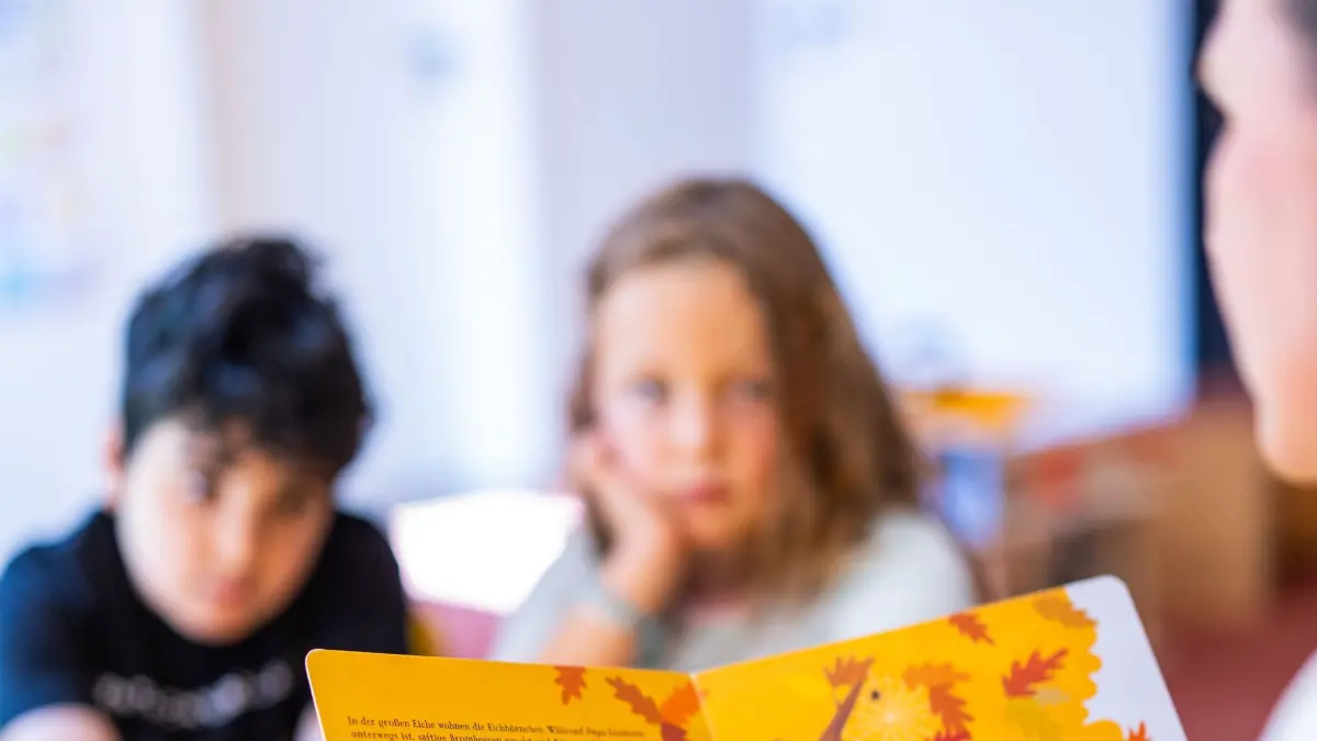 Vorlesetag: PRODUKTION - 12.08.2025, Bremen: Eine Erzieherin liest im Kindergarten zwei Kindern aus einem Buch vor. Der bundesweite Vorlesetag wurde 2004 von der Wochenzeitung «Die Zeit», der Stiftung Lesen und der Deutschen Bahn ins Leben gerufen. Er soll die Begeisterung für das Lesen und Vorlesen wecken und Kinder bereits früh mit dem geschriebenen und erzählten Wort in Kontakt bringen. Foto: Markus Hibbeler/dpa +++ dpa-Bildfunk +++