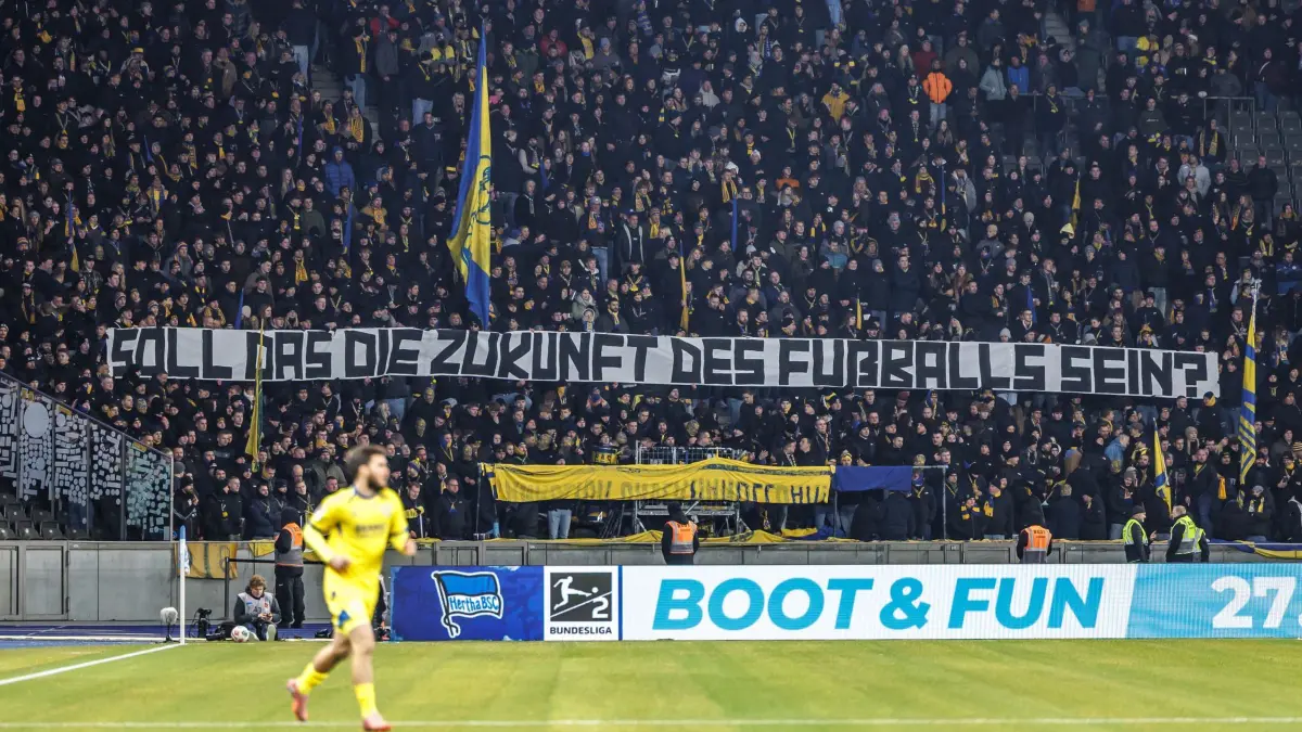 Hertha BSC - Eintracht Braunschweig: 21.11.2025, Berlin: Fußball: 2. Bundesliga, Hertha BSC - Eintracht Braunschweig, 13. Spieltag, Olympiastadion. Fans von Eintracht Braunschweig stehen still hinter einem Banner mit dem Schriftzug "Soll das die Zukunft des Fußballs sein?". Foto: Andreas Gora/dpa - WICHTIGER HINWEIS: Gemäß den Vorgaben der DFL Deutsche Fußball Liga bzw. des DFB Deutscher Fußball-Bund ist es untersagt, in dem Stadion und/oder vom Spiel angefertigte Fotoaufnahmen in Form von Sequenzbildern und/oder videoähnlichen Fotostrecken zu verwerten bzw. verwerten zu lassen. +++ dpa-Bildfunk +++