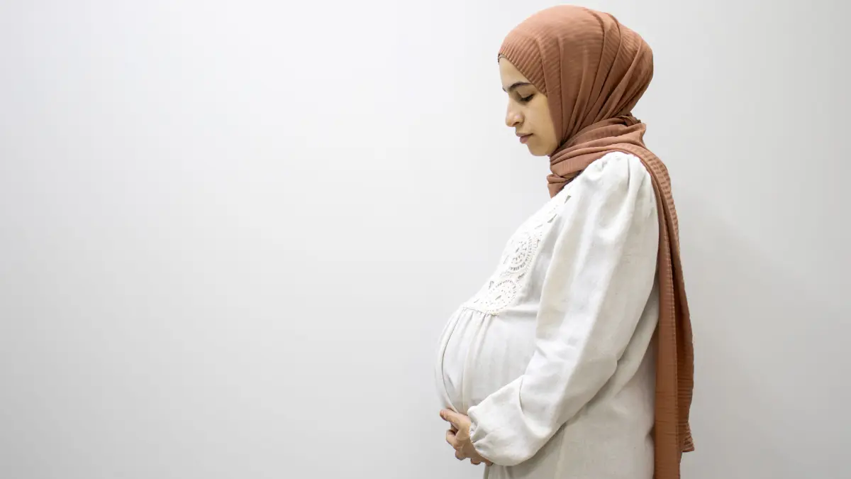 NPG-Lizenz! pregnant Arabic muslim female on isolated white background touching her tummy showing her body shape during 9th month of pregnancy schwanger muslima frau muslimisch islam jung tradition hidschab