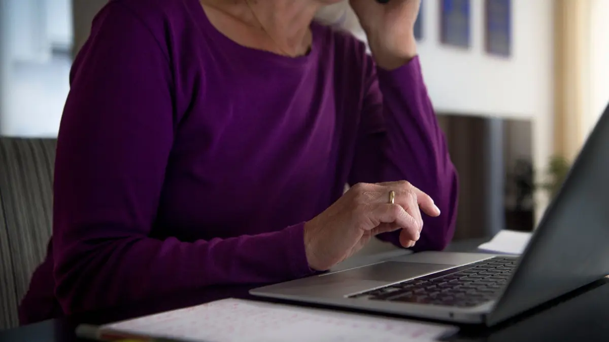 Eine Frau sitzt zu Hause an einem Esstisch am Laptop