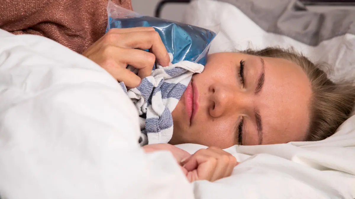 Eine Frau hält sich im Bett einen Kühlakku an die Wange: ILLUSTRATION - Wenn der Zahn einem die Nachtruhe raubt, kann ein Kühlpack im Tuch Linderung verschaffen. (zu dpa: «Warum werden Zahnschmerzen nachts oft schlimmer?») Foto: Christin Klose/dpa Themendienst/dpa-mag - Honorarfrei nur für Bezieher des Dienstes dpa-Magazin +++ dpa-Magazin +++