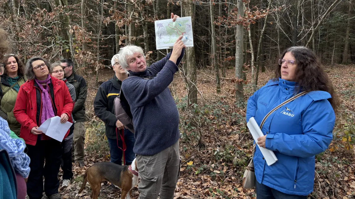 Diplom-Biologe Martin Zorzi, Leiter des Umweltzentrums Landkreis Schwäbisch Hall, hält eine Karte hoch, um den Teilnehmern der Begehung des angedachten Friedwalds die Größe des Gebiets aufzuzeigen. Rechts im Bild ist Brigitte Weingart, Vorsitzende der Nabu-Ortsgruppe Mainhardt.