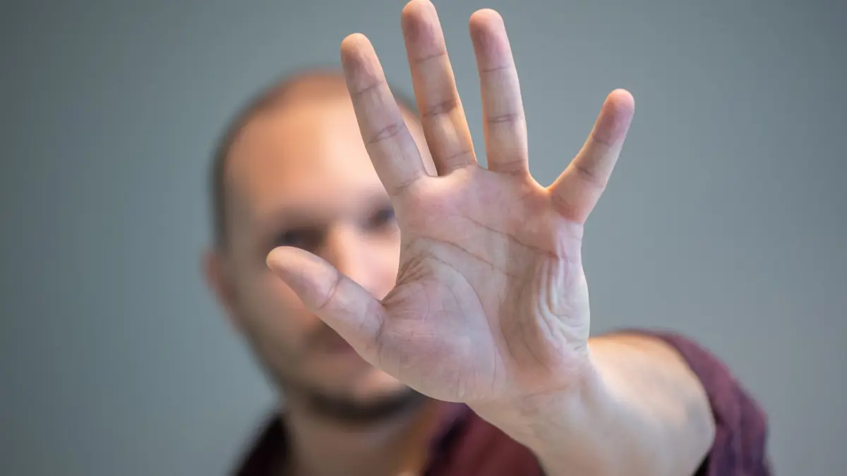 Ein Mann hebt schützend die Hand vor sein Gesicht: ILLUSTRATION - Schwerwiegende Pflichtverletzung: Handgreiflichkeiten am Arbeitsplatz können zur fristlosen Kündigung führen. (zu dpa: «Tritt in Richtung Chef rechtfertigt fristlose Kündigung») Foto: Andrea Warnecke/dpa-mag - Honorarfrei nur für Bezieher des Dienstes dpa-Magazin +++ dpa-Magazin +++