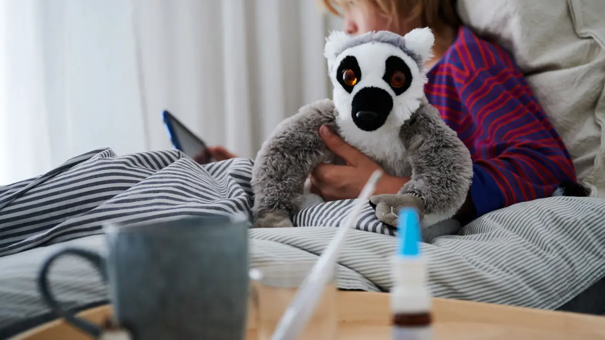 Krankes Kind liegt mit einem Kuscheltier im Bett