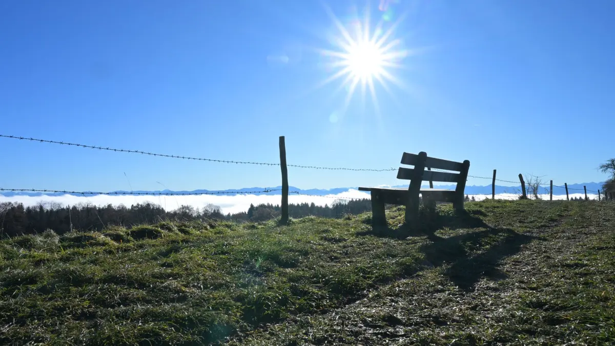 Wetter in Bayern: 02.12.2025, Bayern, Tutzing: Eine Bank für Spaziergänger steht in der Sonne. In der Ferne sind die Alpen zu erkennen. Foto: Malin Wunderlich/dpa +++ dpa-Bildfunk +++