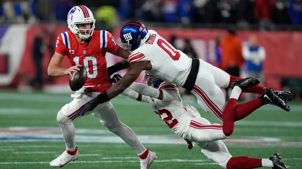 New England Patriots - New York Giants: December 1st, 2025, USA, Foxborough: American Football: NFL professional league, main round, New England Patriots - New York Giants. New England Patriots quarterback Drake Maye (l) runs away from New York Giants cornerback Dru Phillips (bottom) and linebacker Brian Burns (0) in the first half. Photo: Charles Krupa/AP/dpa +++ dpa-Bildfunk +++
