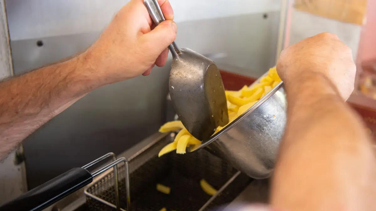 Speiseöl in einer Fritteuse: PRODUKTION - 03.05.2022, Hessen, Frankfurt/Main: Ein Mann schüttet in einem Imbiss Pommes in eine Fritteuse mit Speiseöl. (zu dpa: «Entsorgungsbranche beklagt Altfett-Diebstahl aus Restaurants») Foto: Sebastian Gollnow/dpa +++ dpa-Bildfunk +++