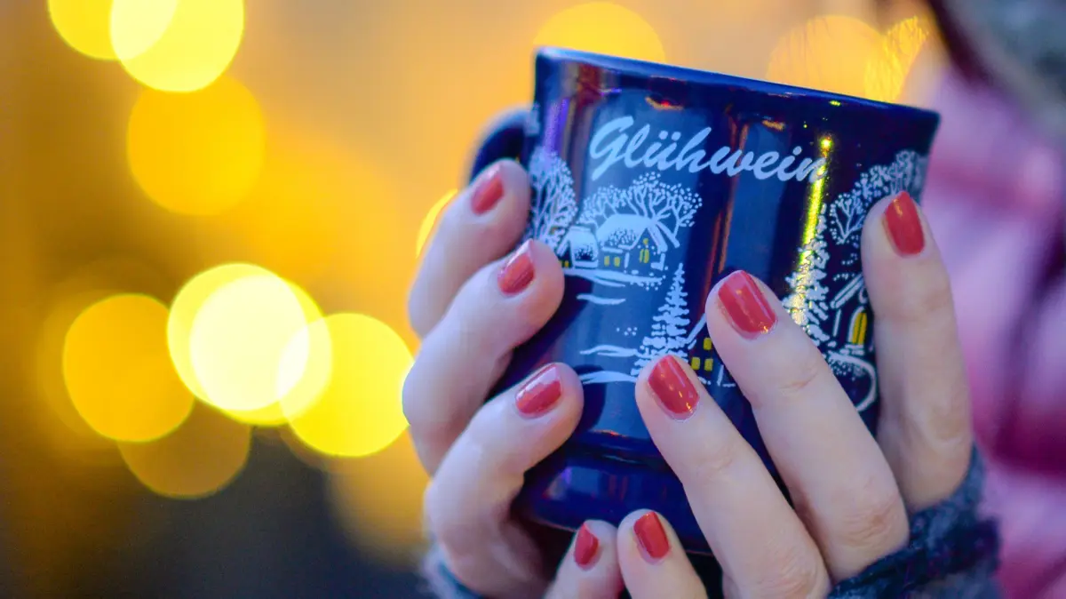 Eine Frau hält auf dem Weihnachtsmarkt eine Tasse mit Glühwein in den Händen.