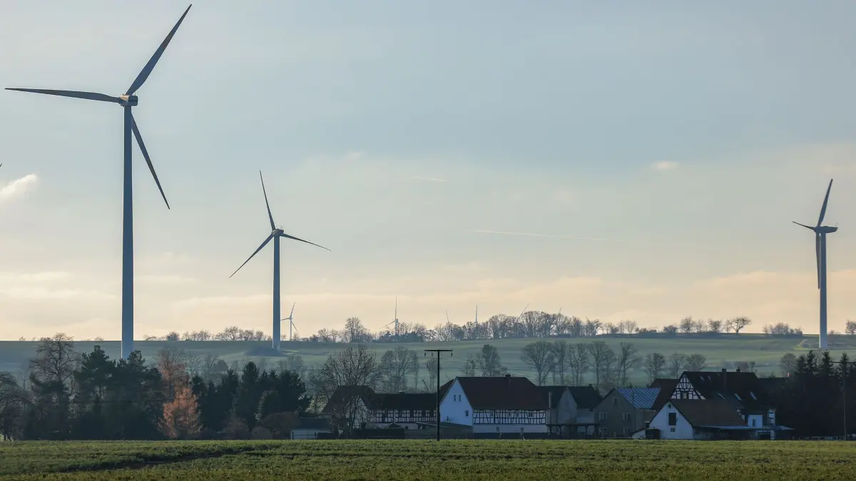 Windräder hinter Dorf: 04.12.2025, Thüringen, Neubraunshain: Mehrere Windkraftanlagen stehen hinter dem kleinen Ort. In Thüringen gelten für Windräder seit 2024 Mindestabstände zu Wohngebieten von 1000 Metern. Foto: Jan Woitas/dpa - Honorarfrei nur für Bezieher des Dienstes ZB-Funkregio Ost +++ ZB-FUNKREGIO OST +++