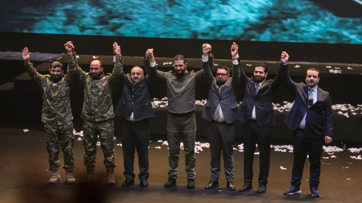 Syrian President Ahmed al-Sharaa (C) and members of his government celebrate during a ceremony at the Convention Center as Syrians celebrate the first anniverasy of the fall of the Assad regime, in the Syrian capital Damascus on December 8, 2025. Tens of thousands took to the streets across Syria on December 8, 2025, to celebrate a year since the toppling of longtime ruler Bashar al-Assad, with President Ahmed al-Sharaa urging people to unite to rebuild the country. Sharaa's Islamist-led alliance launched a lightning offensive in late November last year and took Damascus on December 8 after nearly 14 years of war, ending more than five decades of Assad family rule. (Photo by OMAR HAJ KADOUR / AFP)