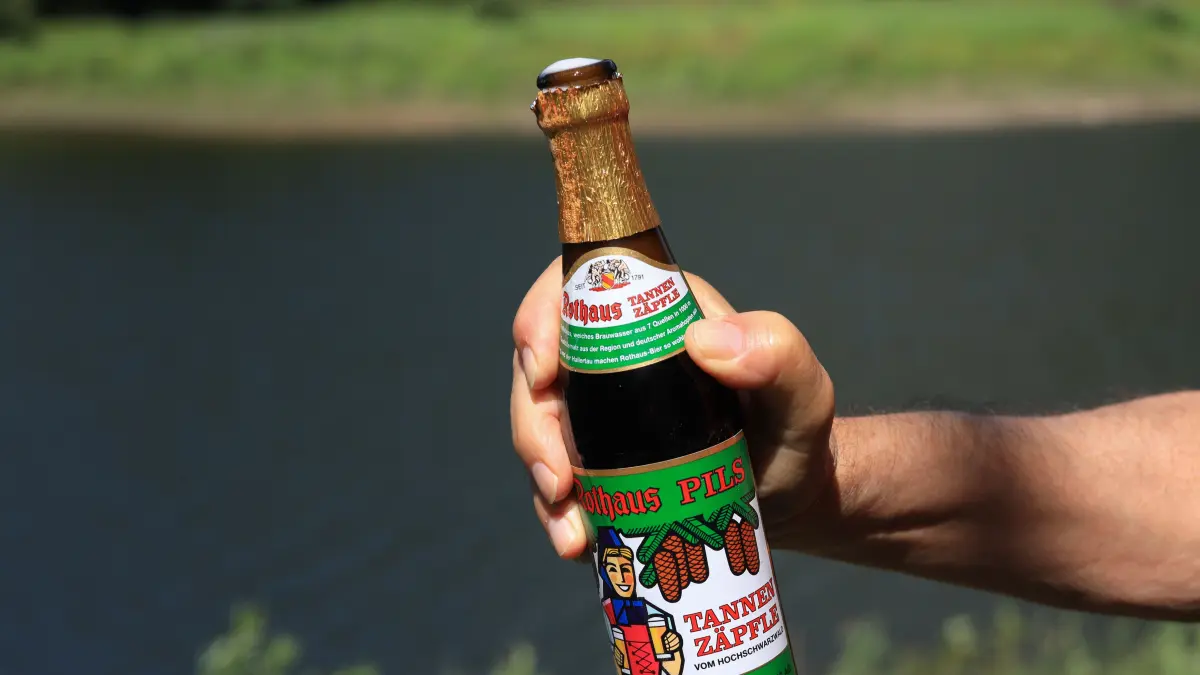 NPG-erweiterte Lizenz / Mantel, Beachten: nur redaktionelle Nutzung! Eine Männerhand hält eine Flasche Rothaus „Tannenzäpfle“-Bier im Freien im Schwarzwald, Deutschland, 23. Juli 2024. Download am 9.12.25 für SWP, Wirtschaft. 895076799 Foto: © Ina Meer Sommer/adobe.stock.com