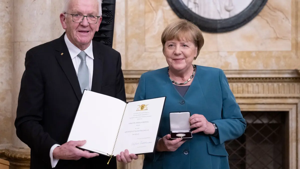 Kretschmann würdigt Merkel für Corona-Politik: 09.12.2025, Baden-Württemberg, Stuttgart: Winfried Kretschmann (Bündnis 90/Die Grünen, l), Ministerpräsident von Baden-Württemberg, überreicht der ehemaligen Bundeskanzlerin Angela Merkel (CDU) im Neuen Schloss die Staufermedaille in Gold. Foto: Marijan Murat/dpa +++ dpa-Bildfunk +++