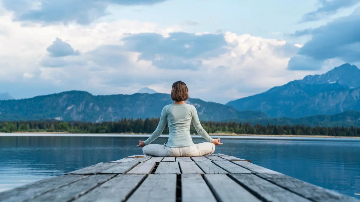 Eine Frau sitzt auf einem Steg und meditiert: ILLUSTRATION - Einfach da sein und bei sich, egal, was um einen herum los ist: Dabei hilft Meditieren, etwa mit der bewährten Bergmeditation. (zu dpa: «Wenn alles zu viel wird: So hilft die Bergmeditation») Foto: Daniel Ingold/Westend61/dpa-tmn - ACHTUNG: Nur zur redaktionellen Verwendung im Zusammenhang mit dem genannten Text und nur bei vollständiger Nennung des vorstehenden Credits - Honorarfrei nur für Bezieher des dpa-Themendienstes +++ dpa-Themendienst +++