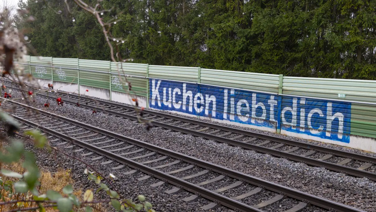 Kuchen - Graffiti auf der Schallschutzwand entlang der Bahngleise in der Nähe des Bahnhofs