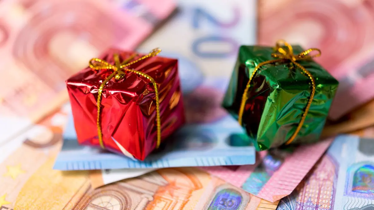 Miniaturweihnachstgeschenke kiegen auf Geldscheinen: ILLUSTRATION - Weihnachtsgeld wird beim Bürgergeld als Einkommen angerechnet: Der Bonus mindert die staatliche Unterstützung im Auszahlungsmonat. (zu dpa: «Weihnachtsgeld erhalten? Warum Ergänzer kaum profitieren») Foto: Monika Skolimowska/dpa/dpa-mag - Honorarfrei nur für Bezieher des Dienstes dpa-Magazin +++ dpa-Magazin +++