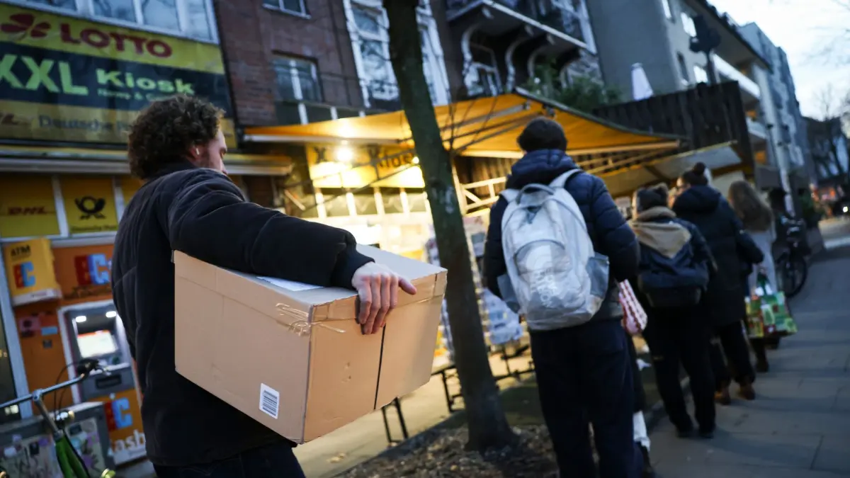 Paketbeförderung: 12.12.2025, Hamburg: Menschen, einige mit Paketen und Päckchen, stehn in einer warteschlange vor einem Post-Kiosk. Foto: Christian Charisius/dpa +++ dpa-Bildfunk +++