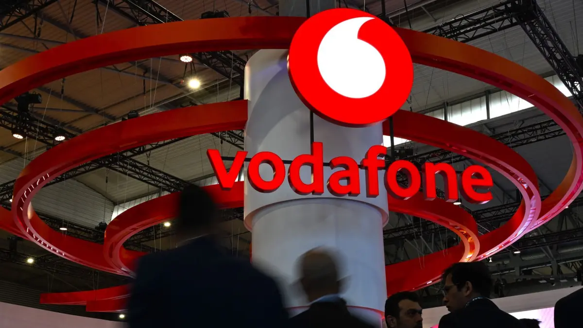 Vodafone-Logo: ARCHIV - 04.03.2025, Spanien, Barcelona: Besucherinnen und Besucher der Mobilfunk-Messe Mobile World Congress (MWC) gehen am Messestand des Telekommunikationskonzerns Vodafone vorbei. Vodafone führt schon am 16. Dezember eine Roaming-Regelung ein, der zufolge Ukrainer in Deutschland mit ihrem ukrainischen Mobilfunkvertrag ohne Zusatzkosten surfen und telefonieren dürfen. (zu dpa: «In Sachen Roaming gehört Ukraine bald zur Europäischen Union») Foto: Wolf von Dewitz/dpa +++ dpa-Bildfunk +++