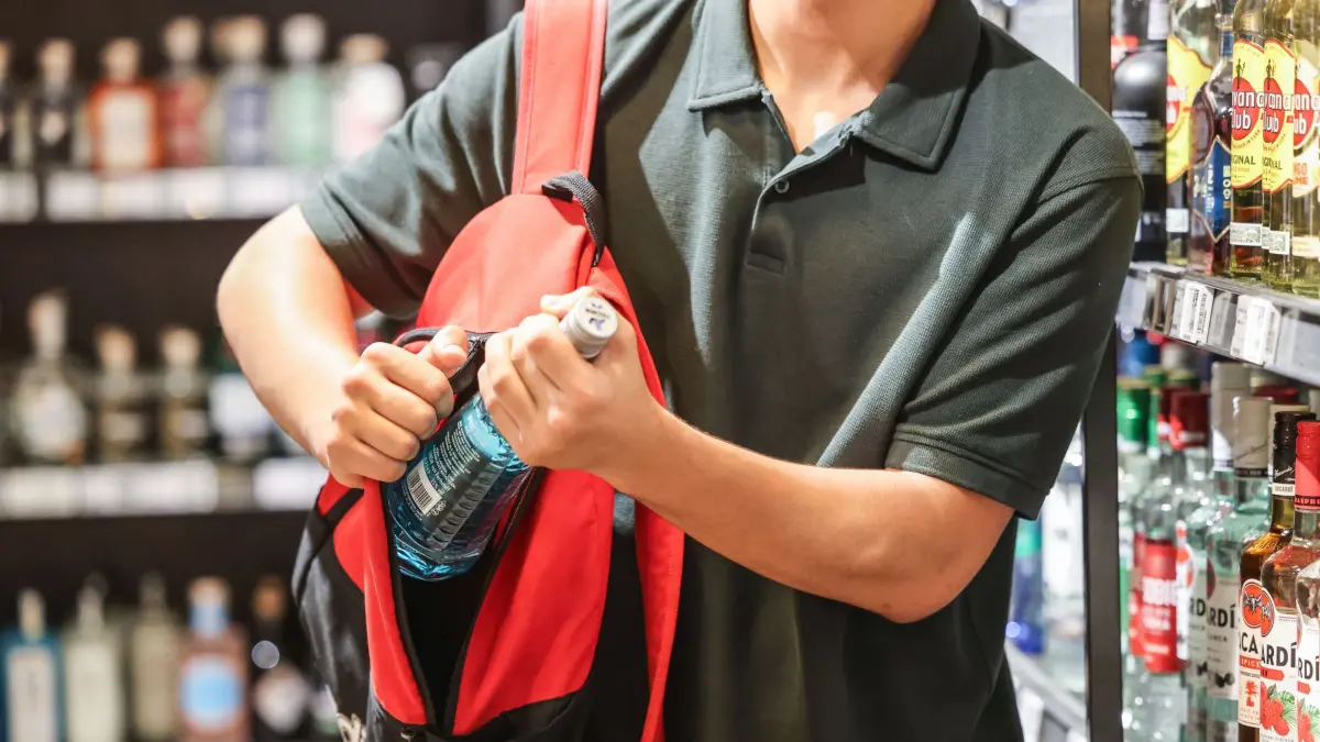 PRODUKTION - 18.06.2025, Nordrhein-Westfalen, Köln: ILLUSTRATION - Ein Mann steckt in einem Supermarkt eine Flasche mit einem Alkoholhaltigen Getränk in seinen Rucksack. (zu dpa: «Kunden klauen mehr - Milliardenschaden durch Ladendiebstahl») Foto: Oliver Berg/dpa +++ dpa-Bildfunk +++