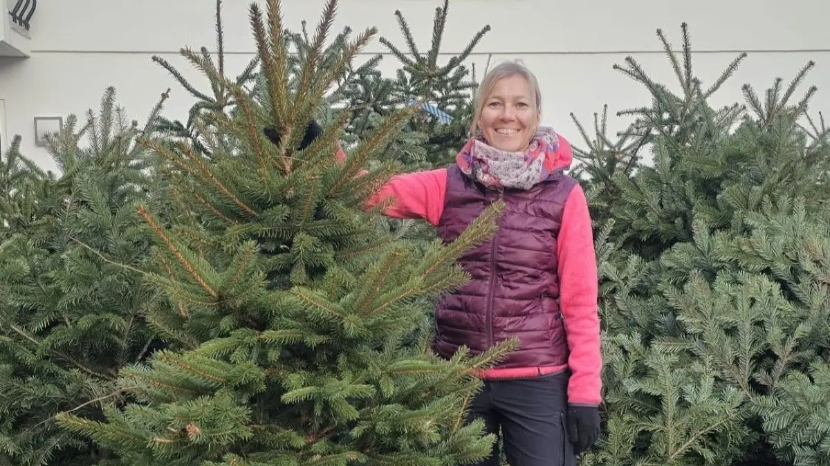 Cornelia Schlegel präsentiert einen Weihnachtsbaum, im Hintergrund liegen noch mehr Bäume. Jetzt fehlt nur noch der Schmuck.