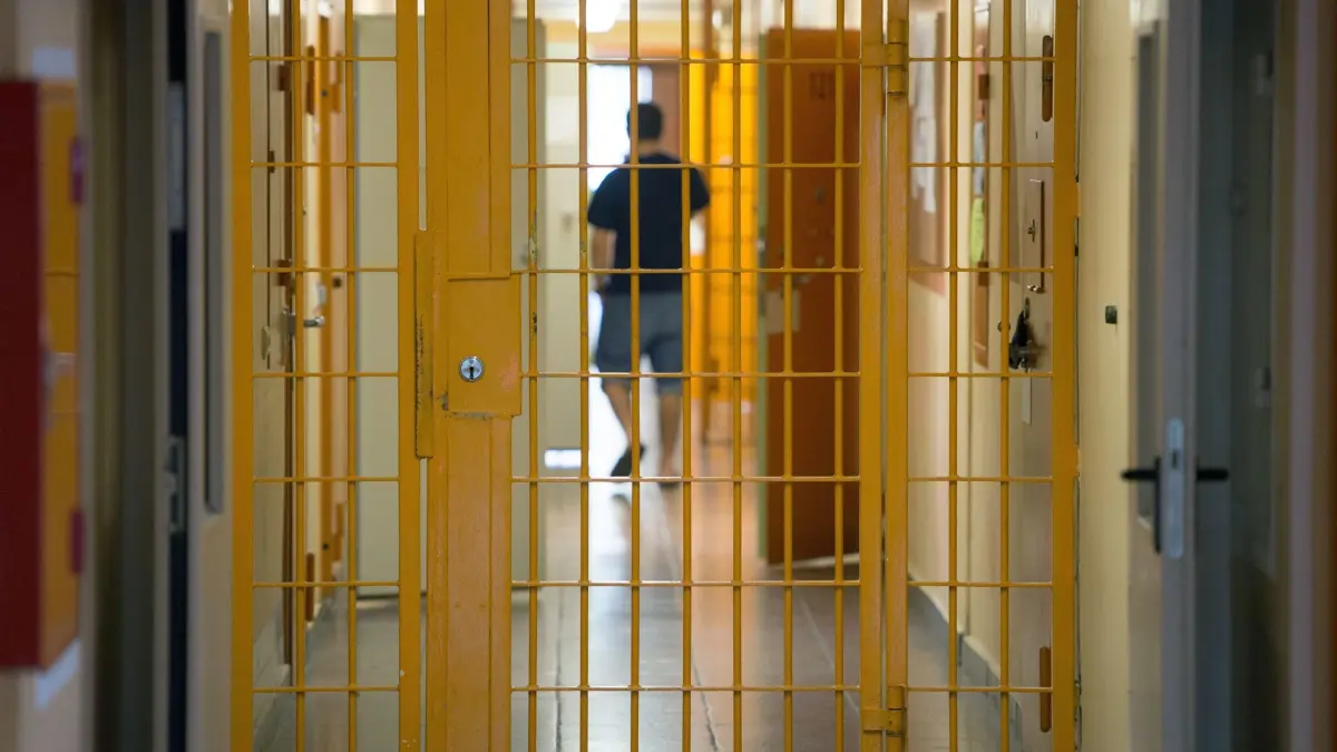 Vergütung für Arbeit hinter Gittern: ARCHIV - 04.09.2015, Thüringen, Hohenleuben: Ein Mann geht in der Justizvollzugsanstalt Hohenleuben hinter einer verschlossenen Gittertür einen Gang entlang. (zu dpa: «Mehr Geld für Arbeit im Gefängnis – Thüringen plant Erhöhung») Foto: Sebastian Kahnert/dpa-Zentralbild/dpa +++ dpa-Bildfunk +++