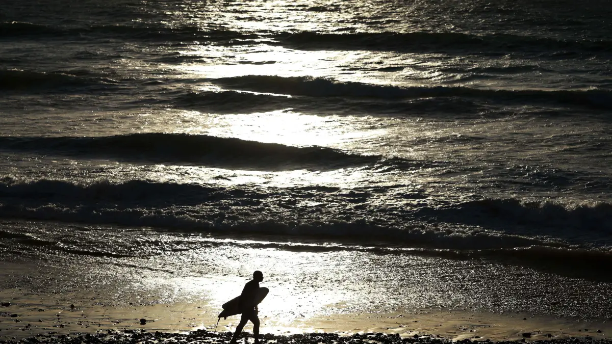 A surfer walks by the sea at Taghzout beach on December 25, 2025. (Photo by FRANCK FIFE / AFP)