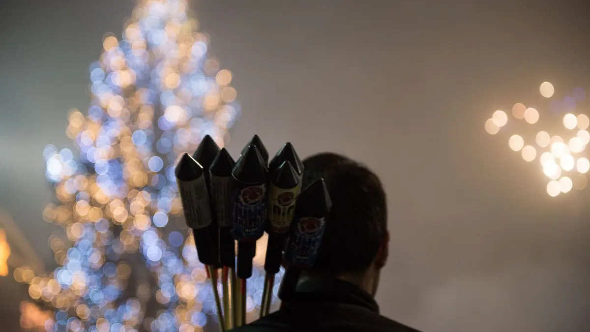 Ein Mann mit Feuerwerksraketen vor einem Weihnachtsbaum: ARCHIV - Ab dem 29. Dezember kann in Deutschland Feuerwerk erworben werden. Beim Transport und der Lagerung sollten Verbraucherinnen und Verbraucher aber einige Vorgaben beachten. (zu dpa: «Worauf bei Kauf und Verwendung von Feuerwerk zu achten ist») Foto: Lino Mirgeler/dpa-mag/dpa - Honorarfrei nur für Bezieher des Dienstes dpa-Magazin +++ dpa-Magazin +++